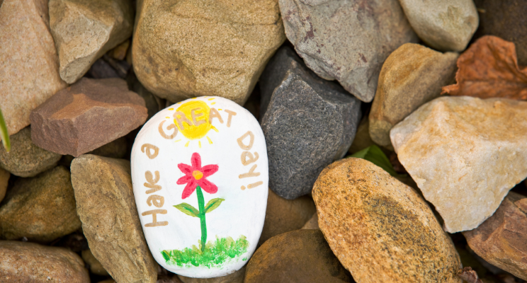 painted rock saying "have a great day" lying amidst plain stones